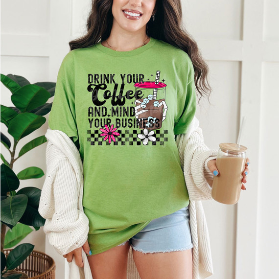 Drink Your Coffee And Mind Your Business DTF Heat Transfer, a woman wearing a green T-shirt with the printed design of a coffee cup and the quote 'Drink Your Coffee And Mind Your Business'