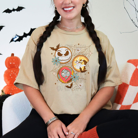 NBC Cookies DTF Heat Transfer, Halloween-themed design on a beige T-shirt featuring a skull, pumpkin, ghost, and spider web with flowers and bats.