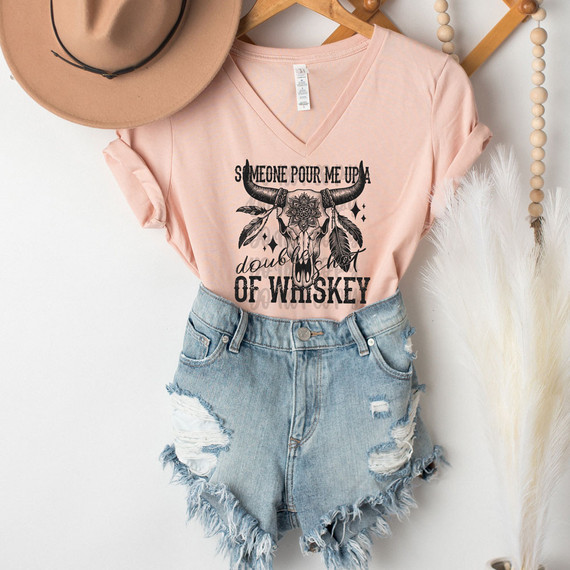 Someone Pour Me A Double Shot Of Whiskey DTF Heat Transfer, a pink V-neck T-shirt with a graphic and text design featuring a bull skull and feathers.