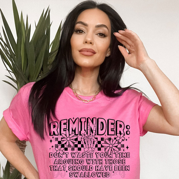 Reminder: Don't Waste Your Time Arguing With Those That Should Have Been Swallowed DTF Heat Transfer, a black and pink graphic design on a pink t-shirt worn by a woman with dark hair, with a plant in the background.