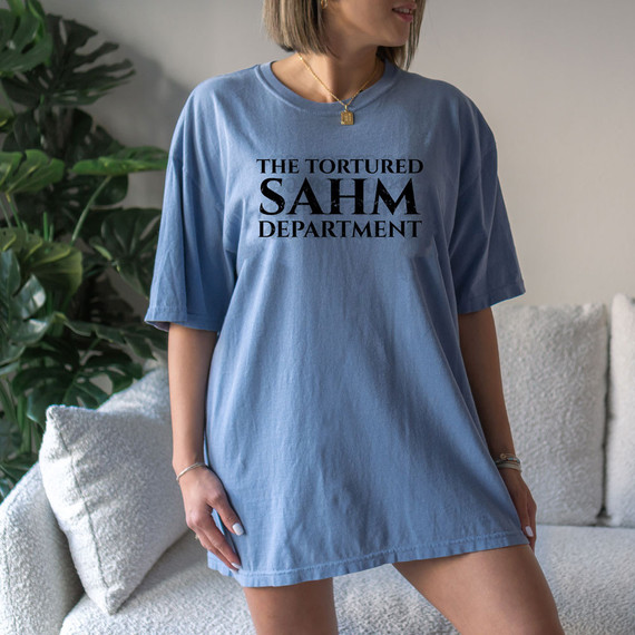 The Tortured SAHM Department DTF Heat Transfer, a woman wearing a blue T-shirt with the black printed text "The Tortured SAHM Department".