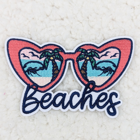 Beaches Sunglasses Embroidered HAT/POCKET Patch, colorful patch featuring sunglasses with a beach scene inside, including palm trees, ocean waves, and a sunset, with the word beaches embroidered at the bottom.