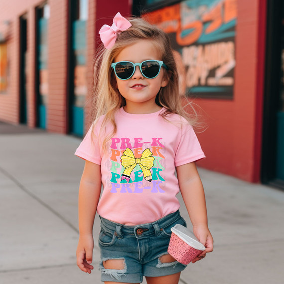 Pre-K Coquette Pencil Bow DTF Heat Transfer, girl wearing pink t-shirt with colorful pre-k design and bow graphics.