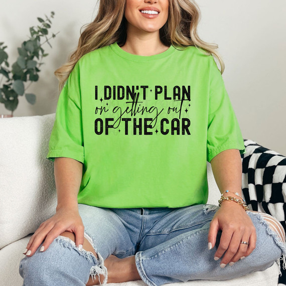I Didn't Plan On Getting Out Of The Car DTF Heat Transfer, a bright green t-shirt featuring this humorous phrase in black text, worn by a woman sitting on a sofa.