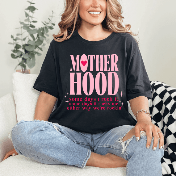 Motherhood Somedays I Rock It DTF Heat Transfer, a pink and black graphic T-shirt worn by a woman with blonde hair, sitting on a couch in a cozy home setting.