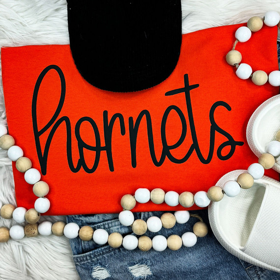 Hornets Black PUFF Screen Print Heat Transfer, displayed on a red fabric with black text, surrounded by a beaded necklace, a black hat, and white shoes.