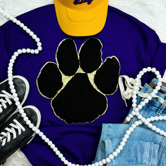 Black Paw with Gold Glitter Chenille Patch, a decorative embroidered patch featuring a black paw print with gold glitter accents, on a purple shirt surrounded by sneakers, jeans, a yellow cap, and a pearl necklace.