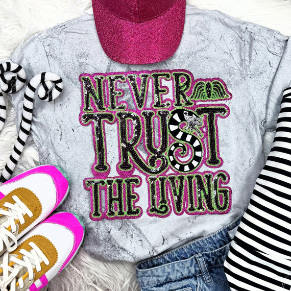 Never Trust The Living Sequin Patch, colorful embroidered patch with words and a snake design on a gray t-shirt, surrounded by striped socks, white and pink sneakers, a pink cap, and a striped shirt.