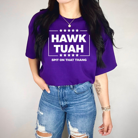 Hawk Tuah WHITE DTF Heat Transfer, a white heat transfer design printed on a purple t-shirt with the text 'HAWK TUAH' and 'SPIT ON THAT THANG'.