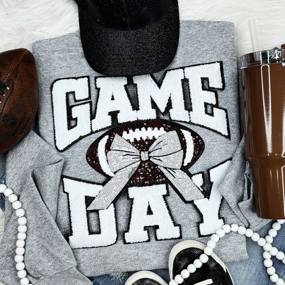 White Chenille Football Game Day with Sequin Bow Patch, close-up of the sweatshirt featuring a football design and bow embellishment, laid out with accessories like a baseball cap, sneakers, and a tumbler
