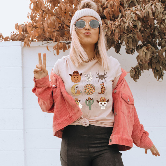 Cowboy Halloween DTF Heat Transfer, woman wearing a Halloween-themed T-shirt with various Halloween icons and making a peace sign.