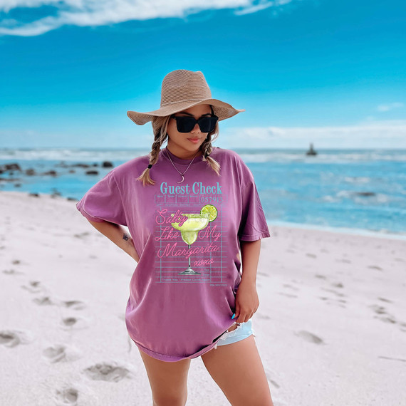 Salty Like My Margarita DTF Heat Transfer, a graphic design featuring a margarita glass with lime on a pink shirt worn by a woman on the beach.