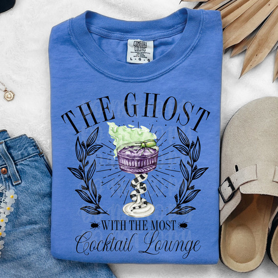 The Ghost With The Most Cocktail Lounge DTF Heat Transfer T-shirt, blue shirt with graphic design of a cocktail glass with green smoke and decorative leaves, and text.