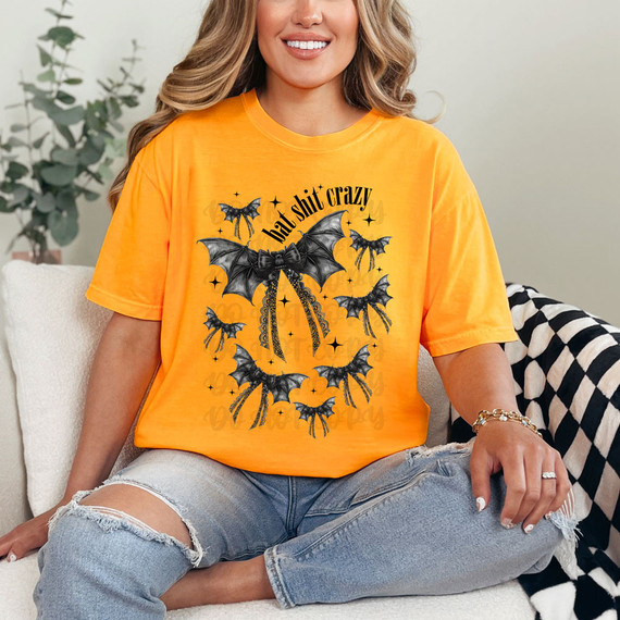 Bat Shit Crazy Coquette DTF Heat Transfer, a vibrant orange T-shirt featuring black bat designs and the phrase 'bat shit crazy' perfect for DIY fashion and crafting.