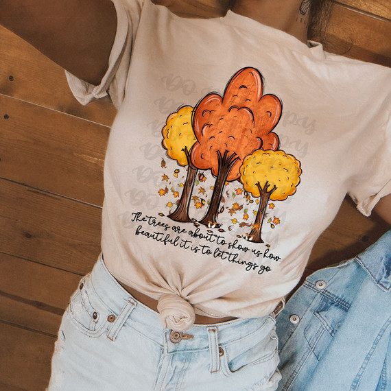 The Trees Are About To Show Us How Beautiful It Is To Let Things Go, product showing a DIY DTF heat transfer on a woman's t-shirt with fall-colored trees and leaves design.