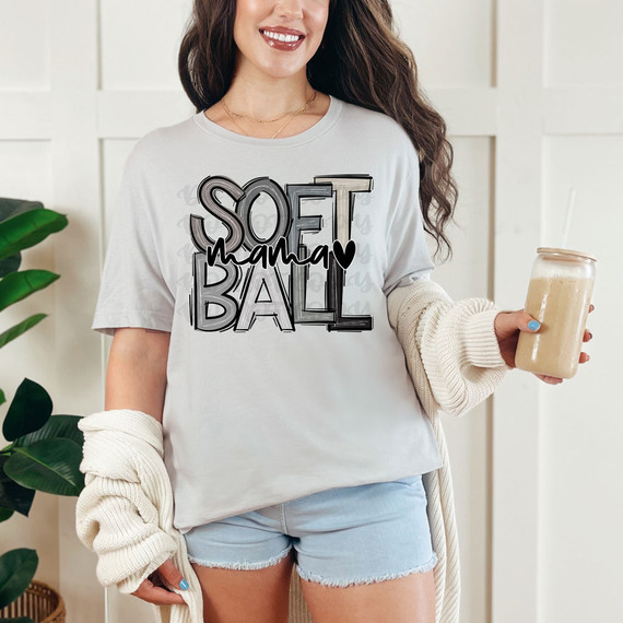 Softball Mama Monochrome DTF Heat Transfer, a woman wearing a white t-shirt with a softball mama graphic design, standing indoors holding a drink.