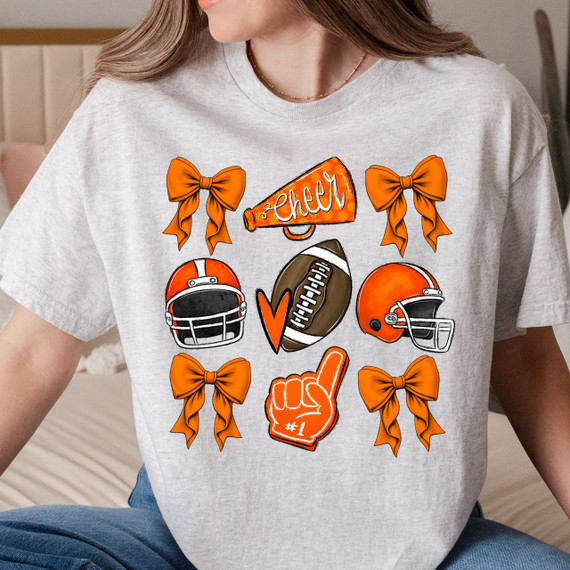 Orange Cheer Bows DTF Heat Transfer, illustration of cheer bows, football helmets, football, cheer megaphone with 'cheer' text, and a hand with #1 foam finger in orange and black colors on a woman's t-shirt.