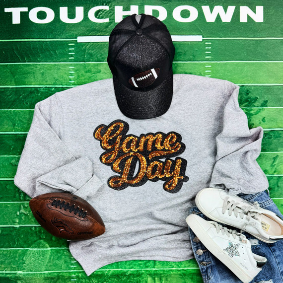 Orange Sequins Game Day Patch, a sparkling orange sequin patch with the words 'Game Day' in bold lettering, displayed on gray sweatshirt with football, sneakers, and cap for football fan or sports enthusiasts.