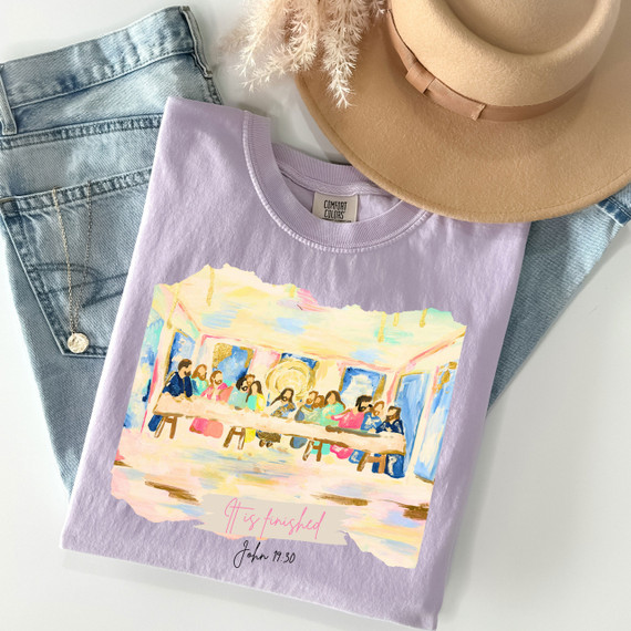 The Last Supper DTF Heat Transfer, colorful artistic print of The Last Supper on a light purple T-shirt with text 'It is finished' and John 19:30, flat lay with denim jeans and a beige hat.