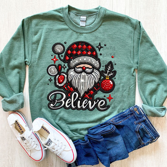 Believe Faux Embroidery DTF Heat Transfer, Christmas-themed sweatshirt with Santa Claus design, red and black plaid hat, white beard, and red ornament, paired with blue jeans and white sneakers.