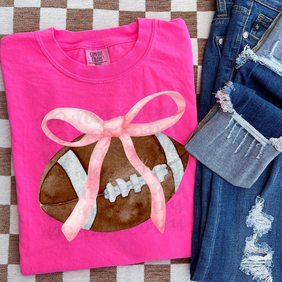 Coquette Football DTF Heat Transfer, pink T-shirt with football design and pink bow, paired with distressed denim jeans.