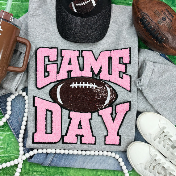 Light Pink Chenille Game Day with Sequin Football Patch, close-up of the embroidered patch on a gray sports t-shirt surrounded by football, shoes, and accessories.
