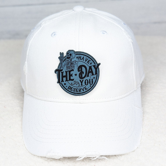 Have The Day You Deserve FAUX Leather Patch, white baseball cap with a blue and black embroidered patch featuring a skeleton bear and the motivational message.