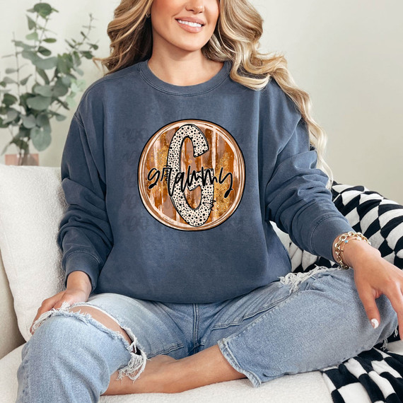 Grammy Fall Brushstrokes DTF Heat Transfer, woman wearing a sweatshirt with a large oval design featuring brushstroke autumn colors, the letter 'G' and the word 'Grammy' in a stylish font.