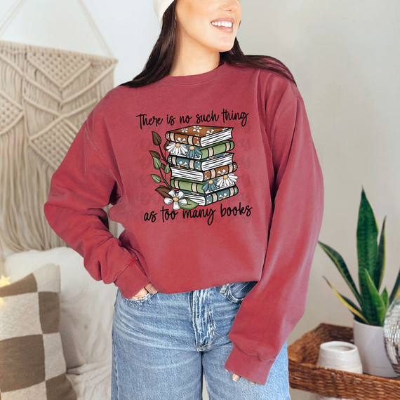 There Is No Such Thing As Too Many Books Fall DTF Heat Transfer, woman wearing a rust-colored sweatshirt with a graphic of stacked books and floral accents.