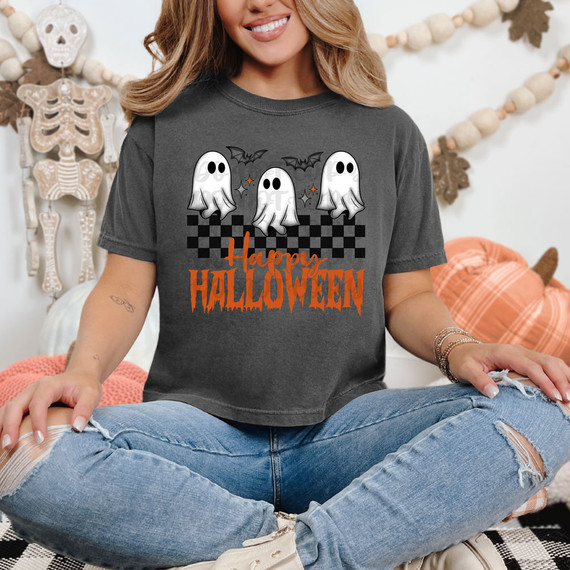 Happy Halloween Ghosts DTF Heat Transfer, a graphic design featuring three cute ghost characters with bats and sparkling accents, and orange Halloween text on a dark gray T-shirt worn by a smiling woman.