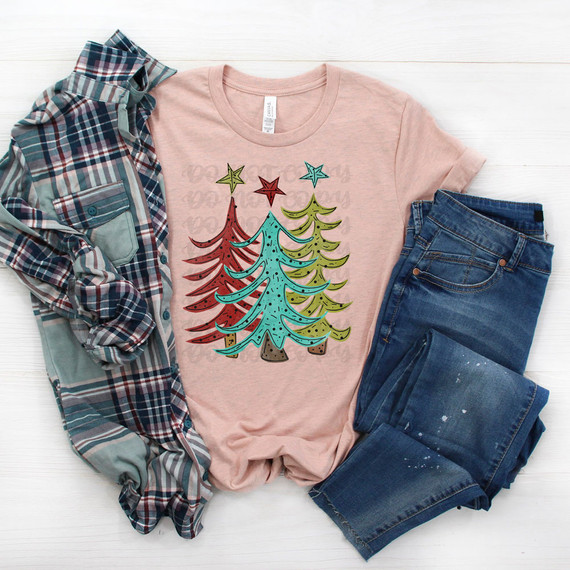 Funky Christmas Trees DTF Heat Transfer, colorful holiday-themed design featuring stylized Christmas trees on a pink t-shirt, with denim and plaid clothing around it.