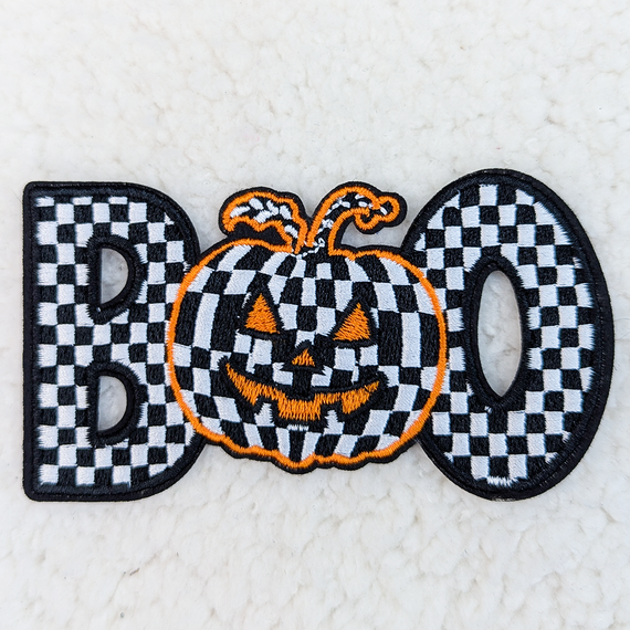 Checkerd BOO Embroidered HAT/POCKET Patch, Halloween-themed patch featuring a pumpkin with a checkered pattern face, orange embroidered outline, and black eyes and mouth.
