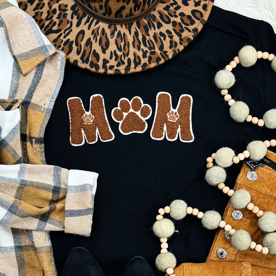 Dog Mom Brown & White Felt with PAW Chenille Embroidered Patch, close-up of a black shirt with the patch and various clothing and accessories around it.