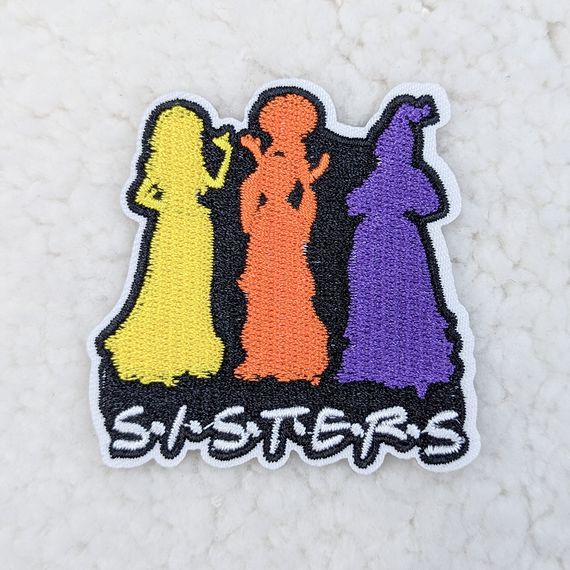 SISTERS Embroidered Hat/Pocket Patch, colorful embroidery featuring three women in yellow, orange, and purple dresses standing side by side with the word 'SISTERS' embroidered below.
