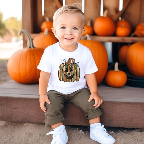 Boy Pumpkin DTF Heat Transfer, young child sitting outdoors, smiling, wearing a pumpkin-themed graphic t-shirt, pumpkins in background