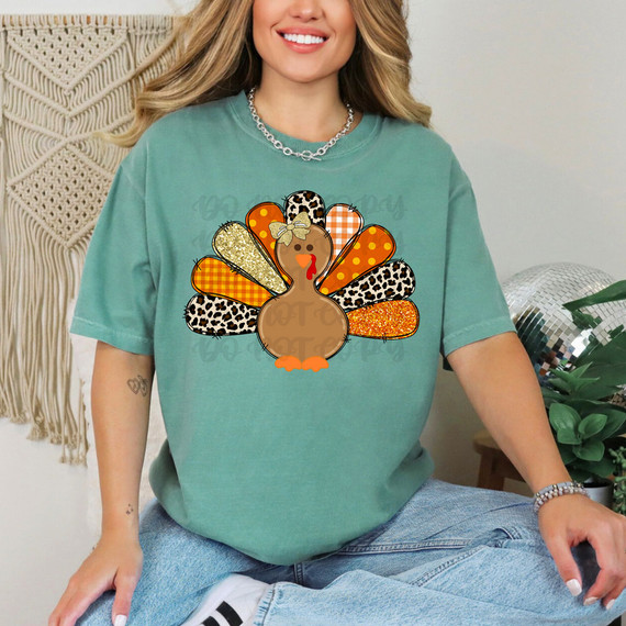 Patterned Turkey DTF Heat Transfer, colorful turkey design with patterned feathers in animal print, glitter, and plaid on a woman's T-shirt.