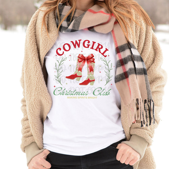 Cowgirl Christmas Club DTF Heat Transfer, white t-shirt with Christmas-themed graphic of cowboy boots with a red bow, surrounded by festive greenery, worn by a person outdoors in winter.