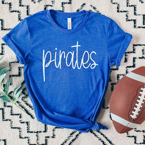 Pirates Mascot WHITE DTF Heat Transfer, product image showing a blue t-shirt with white 'pirates' text, laid on patterned surface with football nearby.