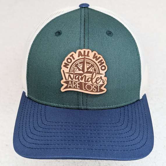 Not All Who Wander Are Lost Leather Hat Patch, humorous patch featuring a compass and the phrase, on a cap with green, white, and blue colors.