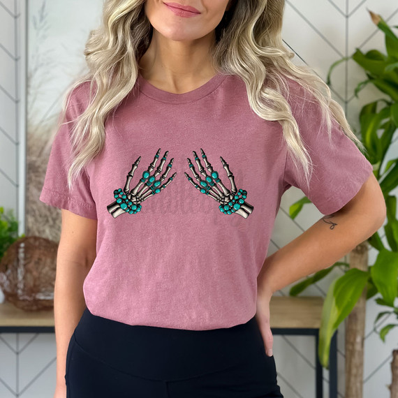 Turquoise Skeleton Hands DTF Heat Transfer, vibrant turquoise skeleton hand decorations on a pink T-shirt worn by a woman.