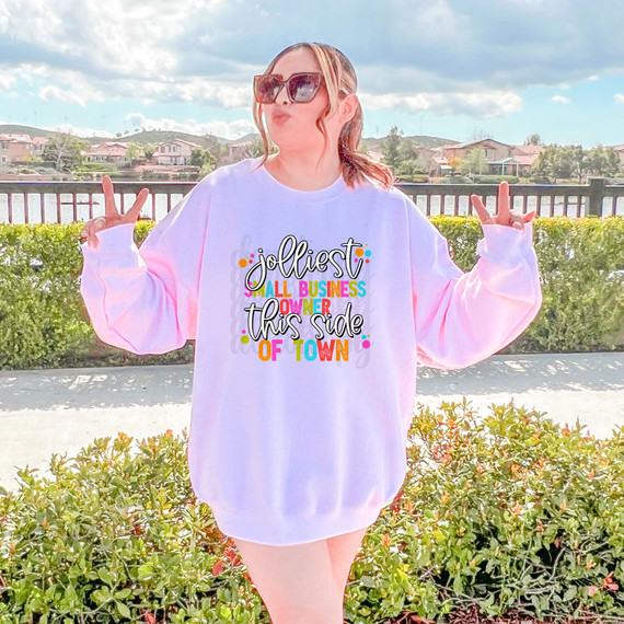 Jolliest Small Business Owner This Side Of Town DTF Heat Transfer, colorful graphic design on a white oversized sweatshirt worn by a woman making peace signs outdoors.