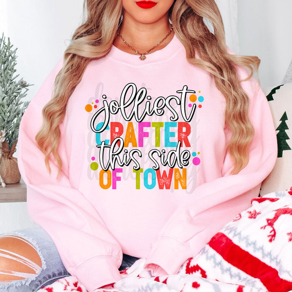 Jolliest Crafter This Side Of Town DTF Heat Transfer, colorful and playful design on a pink sweatshirt featuring the phrase 'Jolliest Crafter This Side Of Town' with multicolored lettering and festive dots.