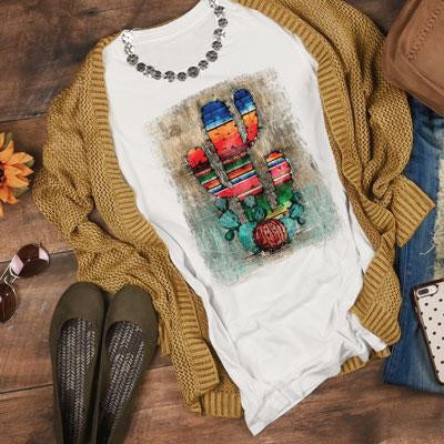 Serape Cactus Sublimation Transfer, colorful cactus design on white T-shirt with a necklace, placed on a cozy brown sweater, shoes, and accessories.