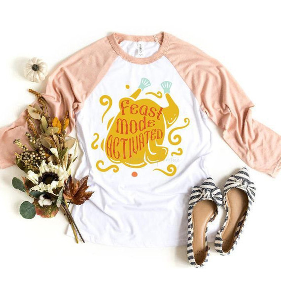 Feast Mode Activated Turkey Sublimation Transfer, a graphic design on a white and pink raglan t-shirt featuring a turkey with festive text, surrounded by decorative elements, ideal for fall and Thanksgiving celebrations.