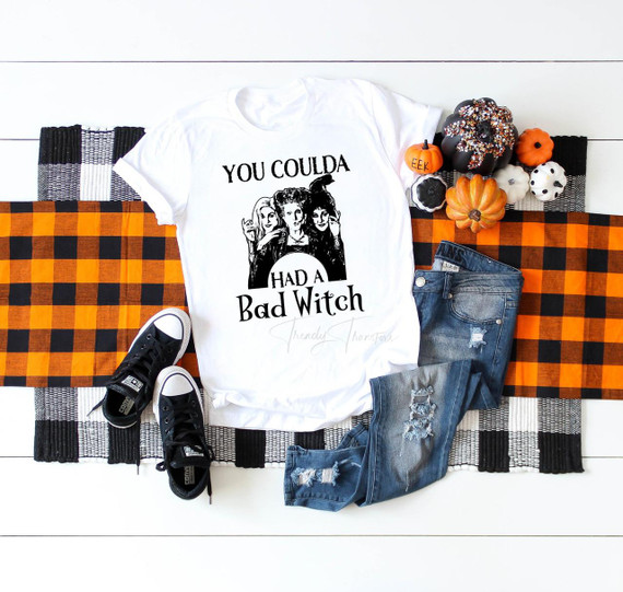 You Coulda Had a Bad Witch Hocus Pocus Sublimation Transfer, a white T-shirt with black text and images of three women, displayed on a checkered black and orange tablecloth with small pumpkins and black and white sneakers.