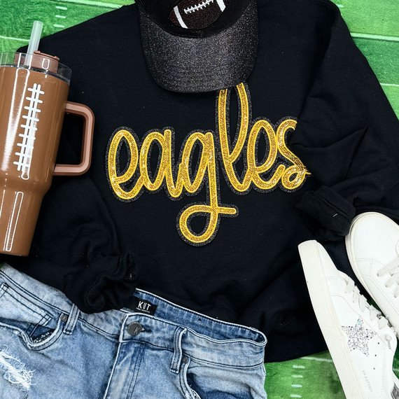 Eagles Gold Sequin Patch, a gold glittery embroidered patch in the shape of the word 'eagles' on a black sweatshirt.