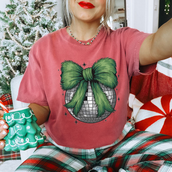 Green Furry Bow Disco Ball DTF Heat Transfer, green furry bow decoration on a disco ball design on a pink T-shirt worn by a woman, holiday Christmas theme.