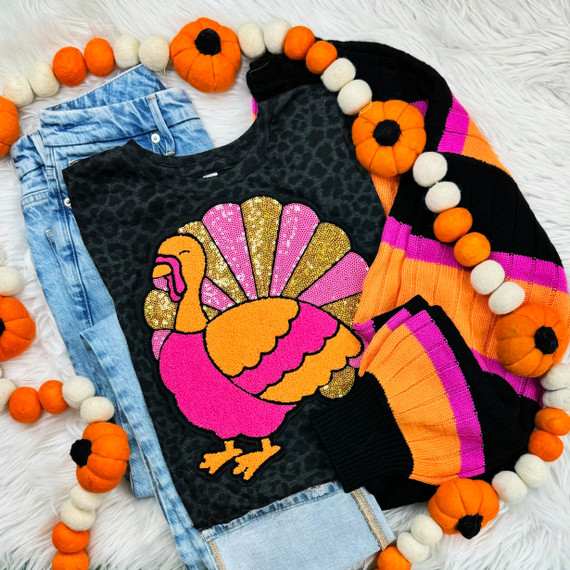 Pink Sequin Turkey Patch, colorful felt turkey patch with sequins on black fabric, paired with blue denim jeans and a black, orange, pink, and purple striped sweater, decorated with a pumpkin garland.