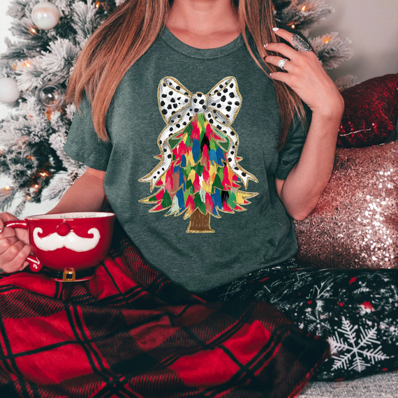 Colorful Brushstroke Christmas Tree Faux Glitter DTF Heat Transfer, a vibrant and festive Christmas tree design with a bow on top, on a woman's t-shirt during holiday celebration.