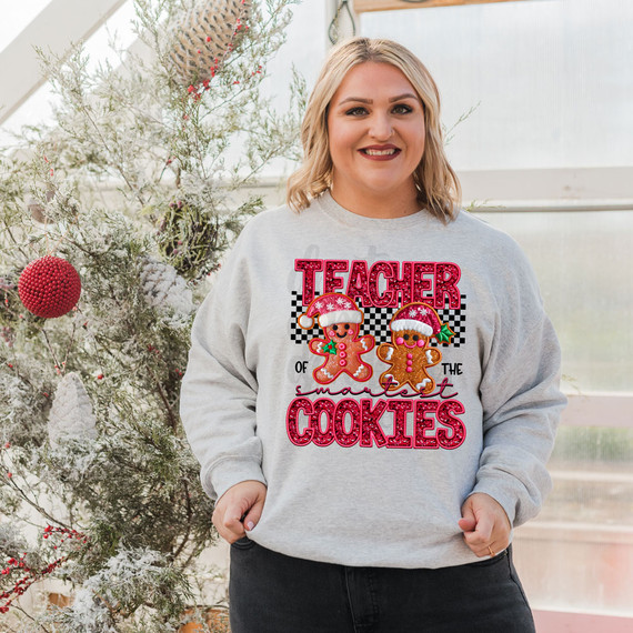 Teacher Of The Smartest Cookies Faux Sequins DTF Heat Transfer, a woman wearing a festive sweatshirt with gingerbread man graphics and holiday hats.